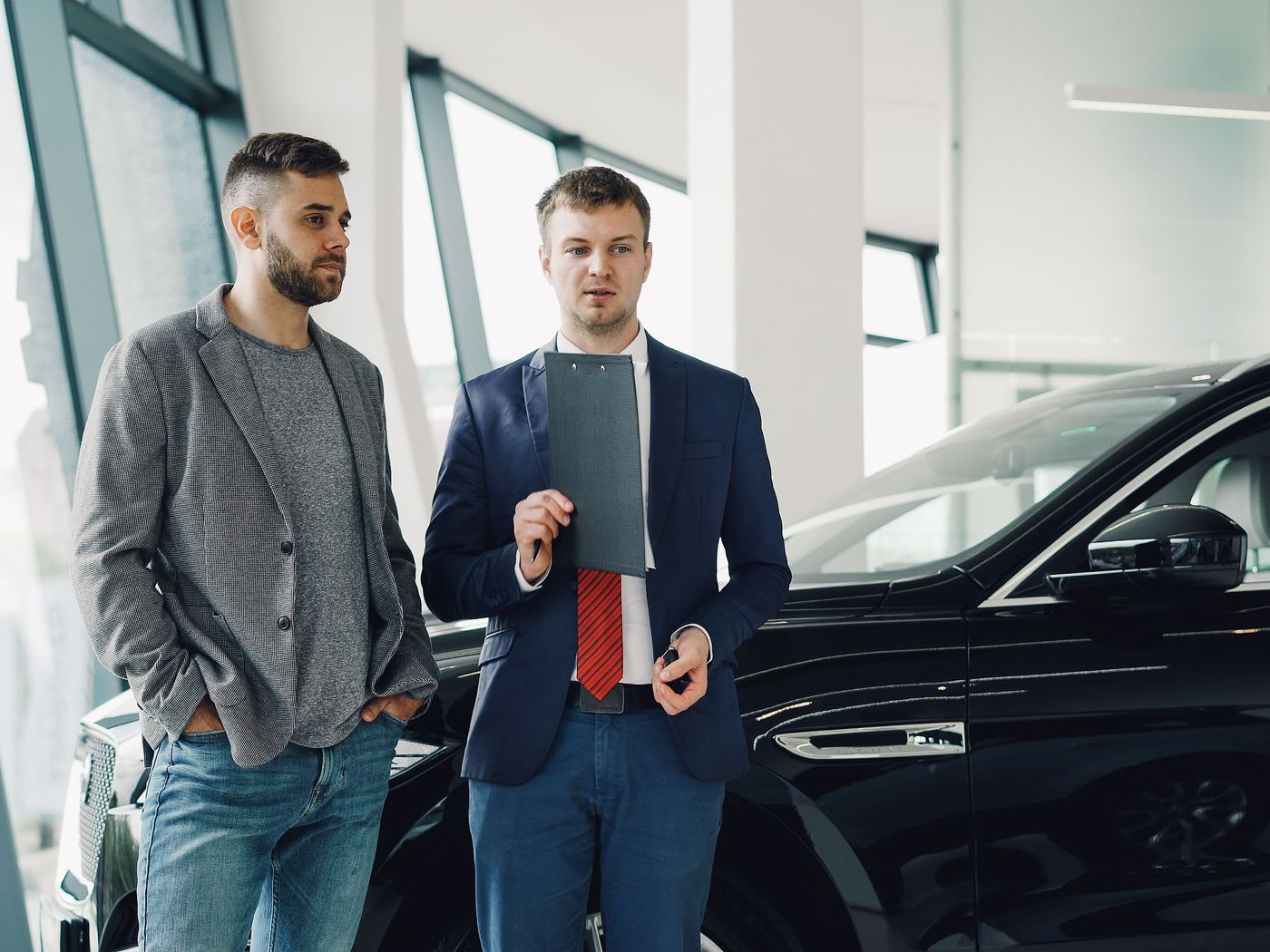 A sales manager with a clipboard talking to a salesperson on the showroom floor.