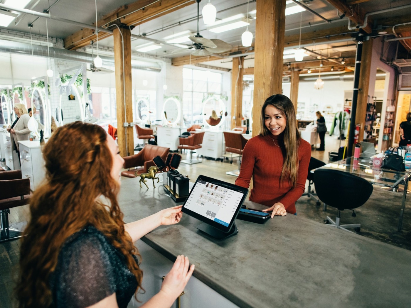 An assistant behind a salon counter smiling with the customer she is serving.