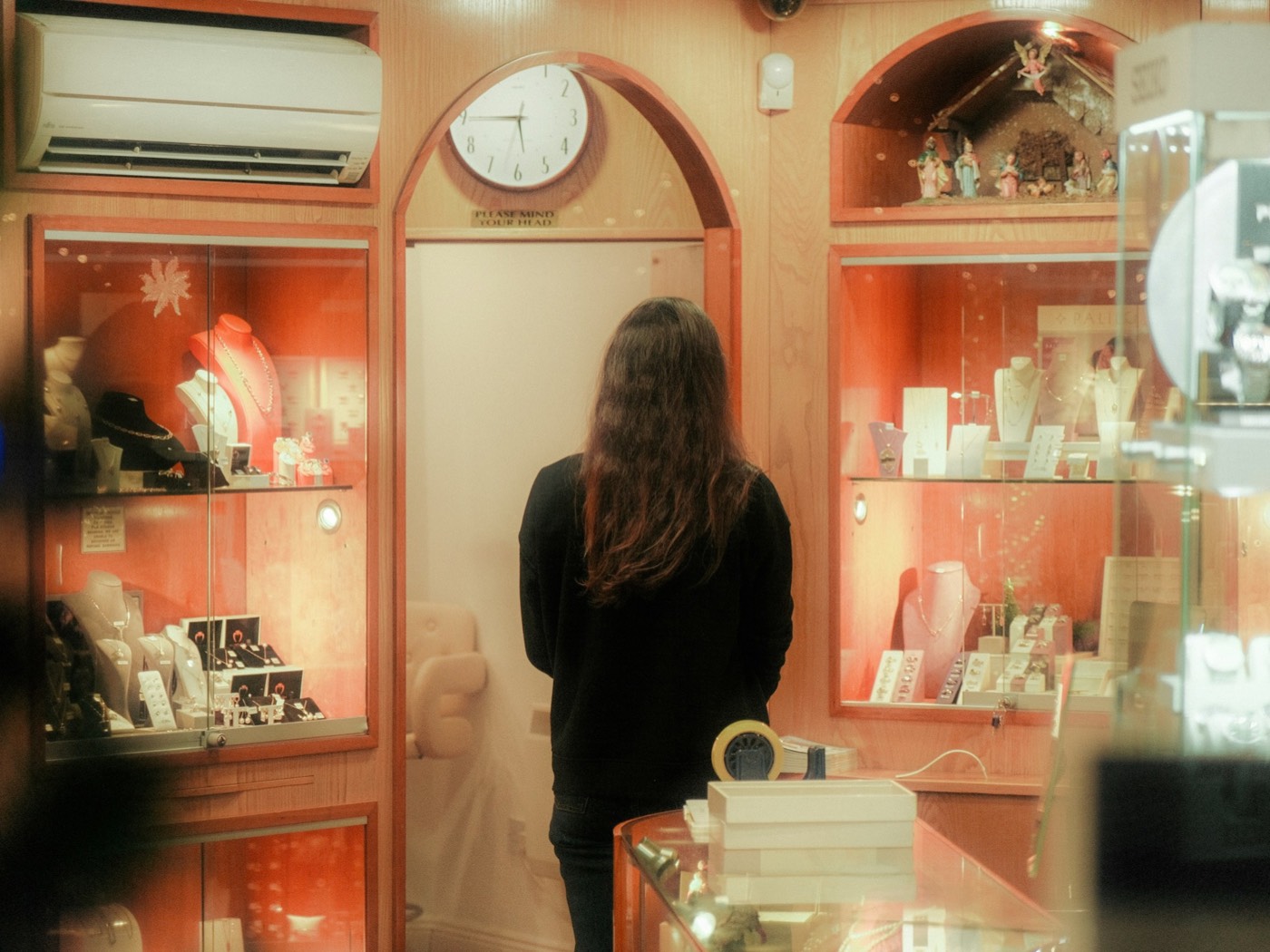A customer standing alone in front of the lit display cases of a jewellery shop.